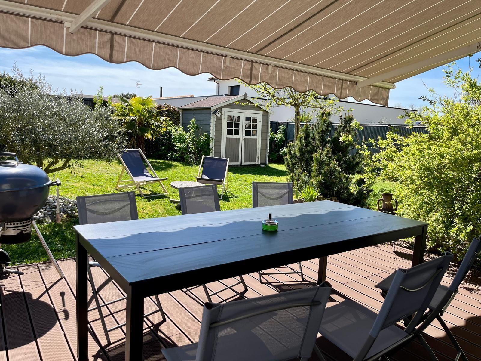 An outdoor patio with a table and chairs, a grill, and a shed in the background.