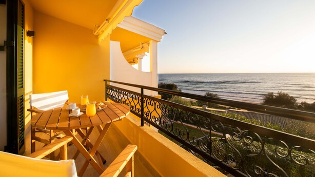 Un balcone con tavolo e sedie in legno, una panca imbottita bianca e vista sul mare.