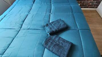 Un lit avec une couette bleue et deux oreillers, l’un orné d’un motif floral et l’autre d’un motif texturé, adossé à un mur de briques.