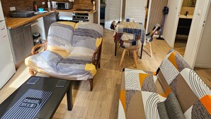 Un salon moderne avec un canapé, une table basse et un téléviseur. Il y a un coin cuisine équipé d’un four à micro-ondes et d’une bouilloire. La pièce est dotée d’un plancher en bois et d’un mur à rayures.