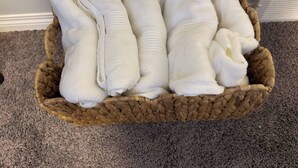 Una cesta tejida llena de toallas blancas sobre un piso alfombrado.