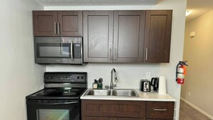 Una cocina compacta con armarios de madera oscura, un microondas de acero inoxidable, una estufa negra y un lavamanos con grifo.