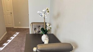 Un comedor con una mesa oscura, un jarrón blanco con flores y un sillón de cuero tapizado.