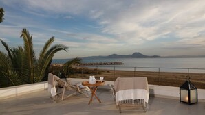 Eine Terrasse mit Meerblick, ein Tisch mit Wasserkrug und Tasse sowie Liegestühle.