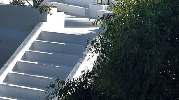 Eine weiße Treppe führt zu einem Gebäude mit einem Strohdach und Laternen, mit Blick auf die Küste.