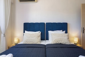 Ein Doppelbett mit dunkelblauem Kopfteil, weißen Kissen mit dekorativen Mustern und einer gesteppten dunkelblauen Bettdecke. Es gibt zwei Nachttische mit Lampen.