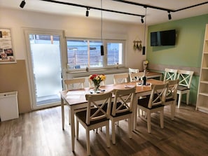 A dining area with a wooden table, white chairs, and a window with blinds.