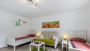 A modern, well-lit room with a sofa, a green armchair, a small table with decorative items, and a painting of red flowers on the wall.