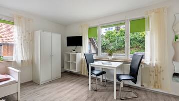 Ein Zimmer mit einem weißen Kleiderschrank, einem Schreibtisch mit zwei Stühlen, einem Fernseher und einem Fenster mit Blick auf Grünflächen.