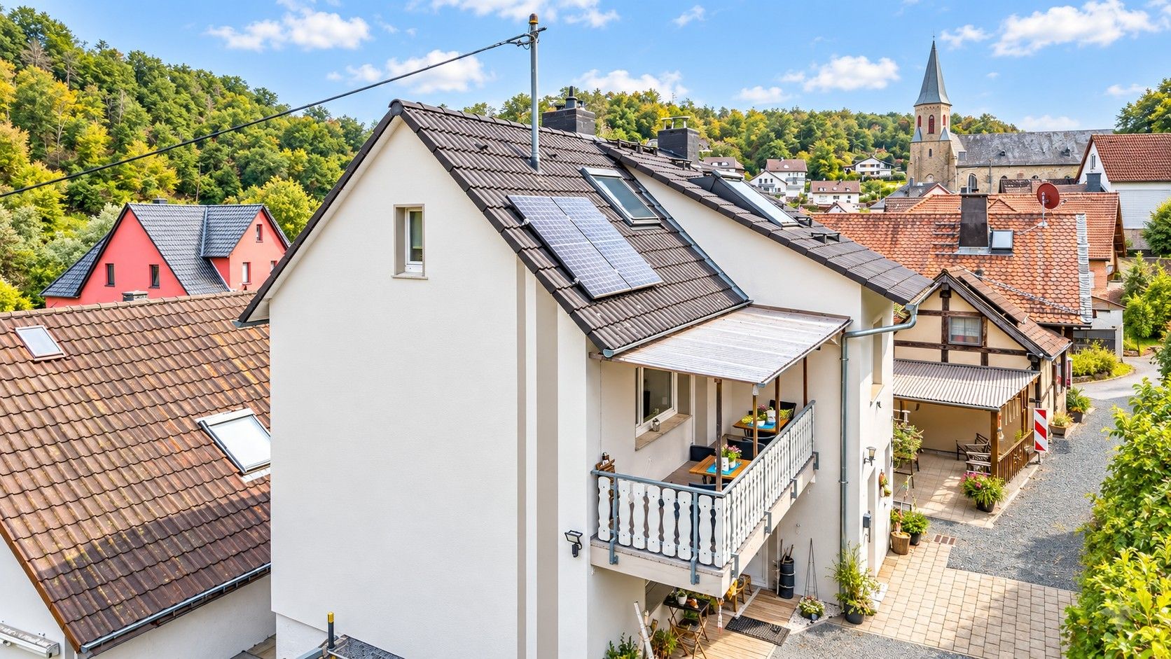 Ein Wohngebäude mit Balkon, Solaranlage und Blick auf eine Kirche im Hintergrund.