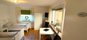 A compact room with a bed, a small table, a wardrobe, and a window with a heart decoration.