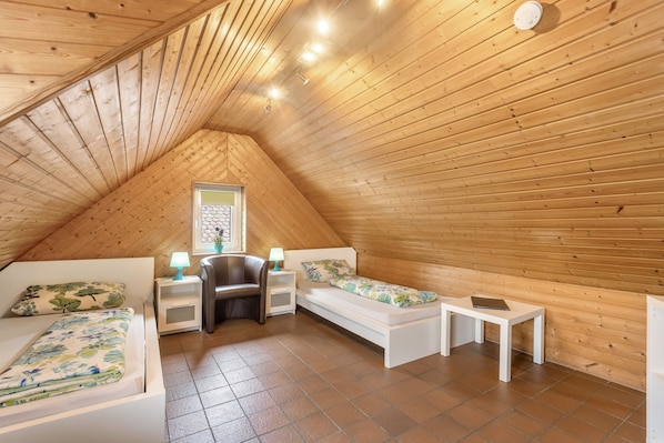 A cozy attic bedroom with a sloped ceiling, a bed, a sofa, a small table, and a nightstand with lamps.