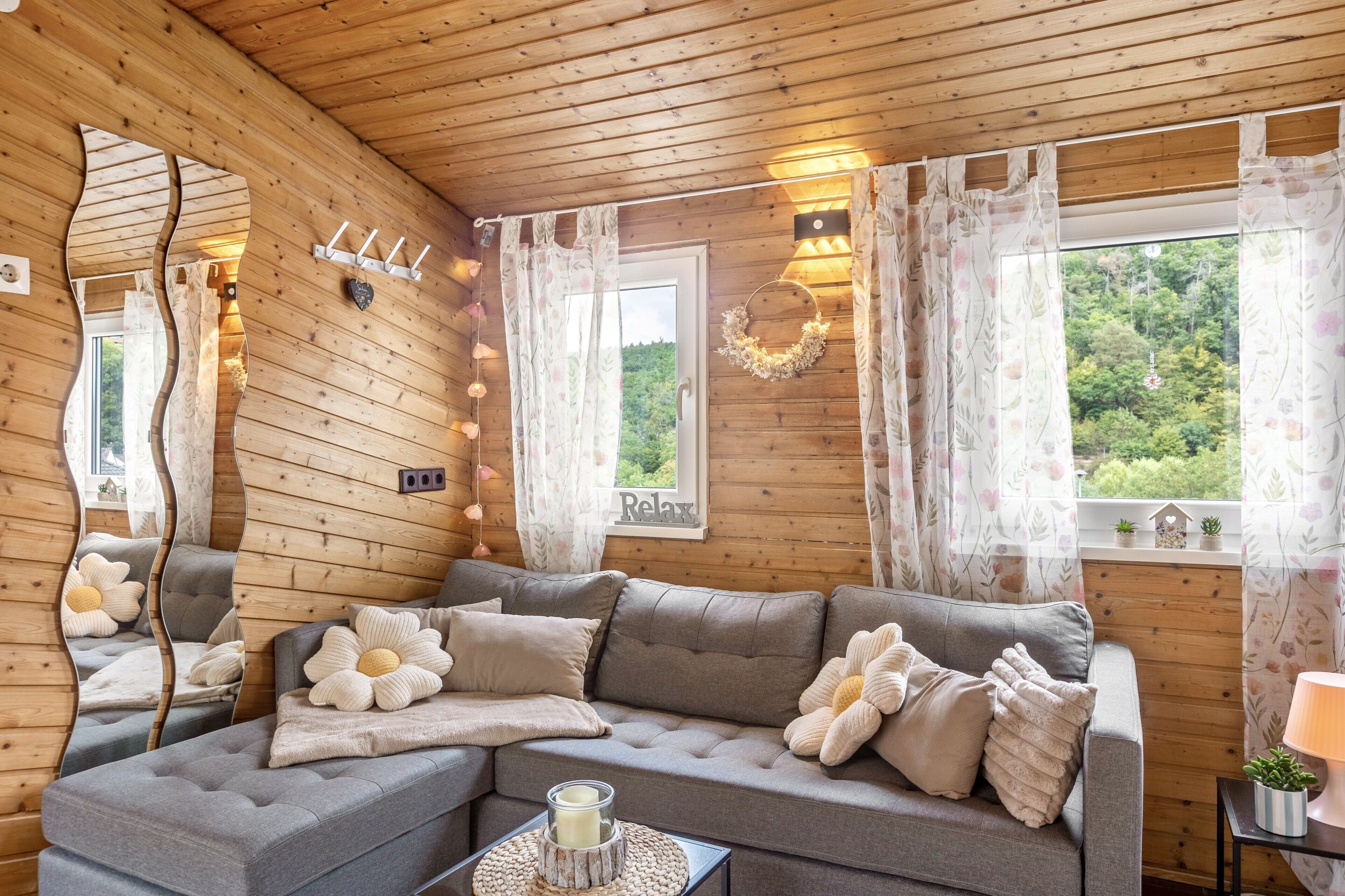 Ein gemütliches Blockhaus-Interieur mit einer Eckcouch, einem Spiegel und Blick auf die grüne Umgebung.