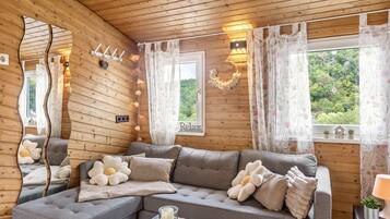 Ein gemütliches Blockhaus-Interieur mit einer Eckcouch, einem Spiegel und Blick auf die grüne Umgebung.