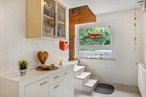 A staircase leading to a landing with a view of greenery outside, a white cabinet with drawers, a small plant, and a decorative item resembling a heart. - Holiday Home "Zum Burgfried" with Castle View, Private Terrace, and Wi-Fi (Usingen)