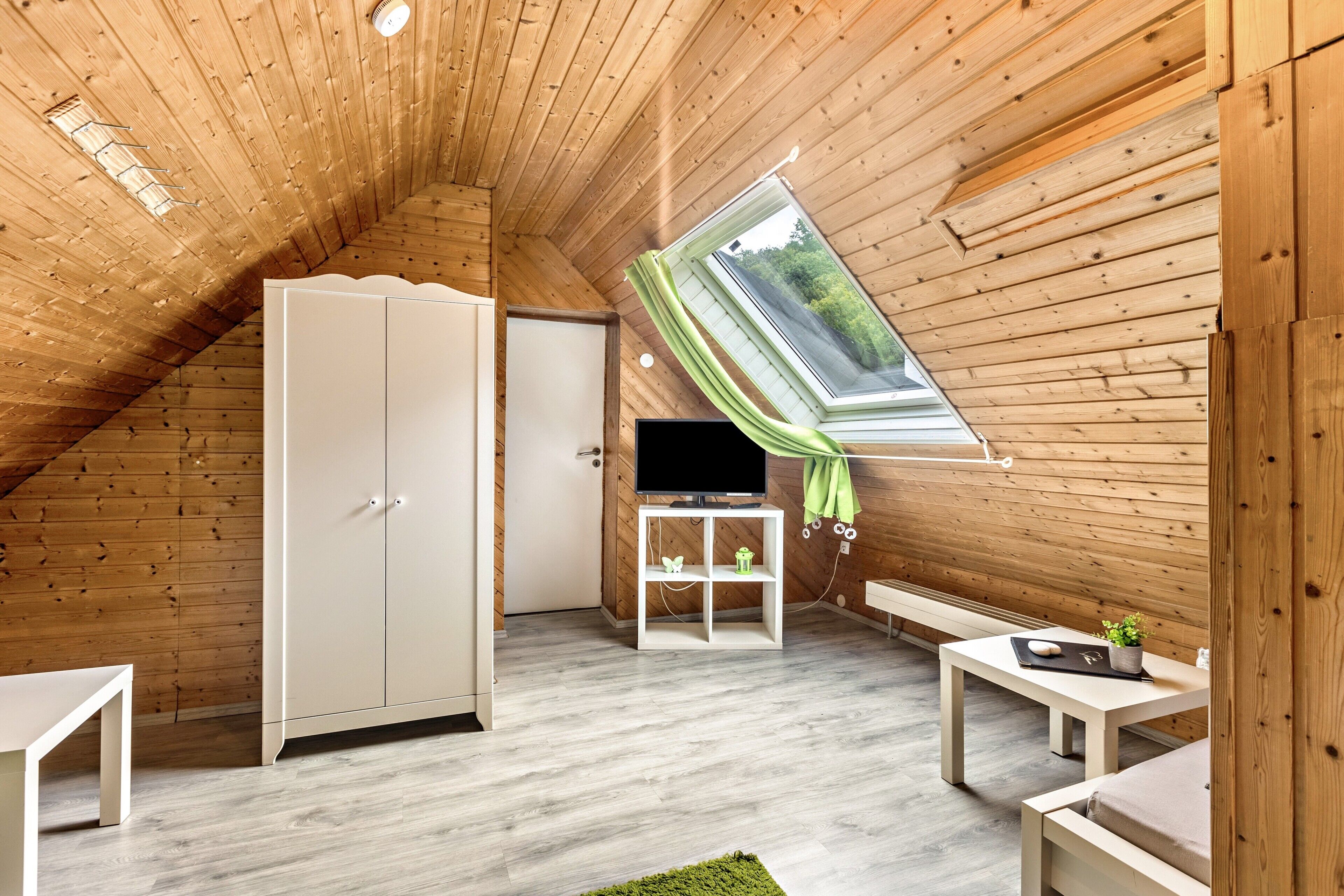 Une pièce mansardée chaleureuse avec des murs en bois, un plafond en pente, une armoire, un téléviseur, une petite table et un banc.