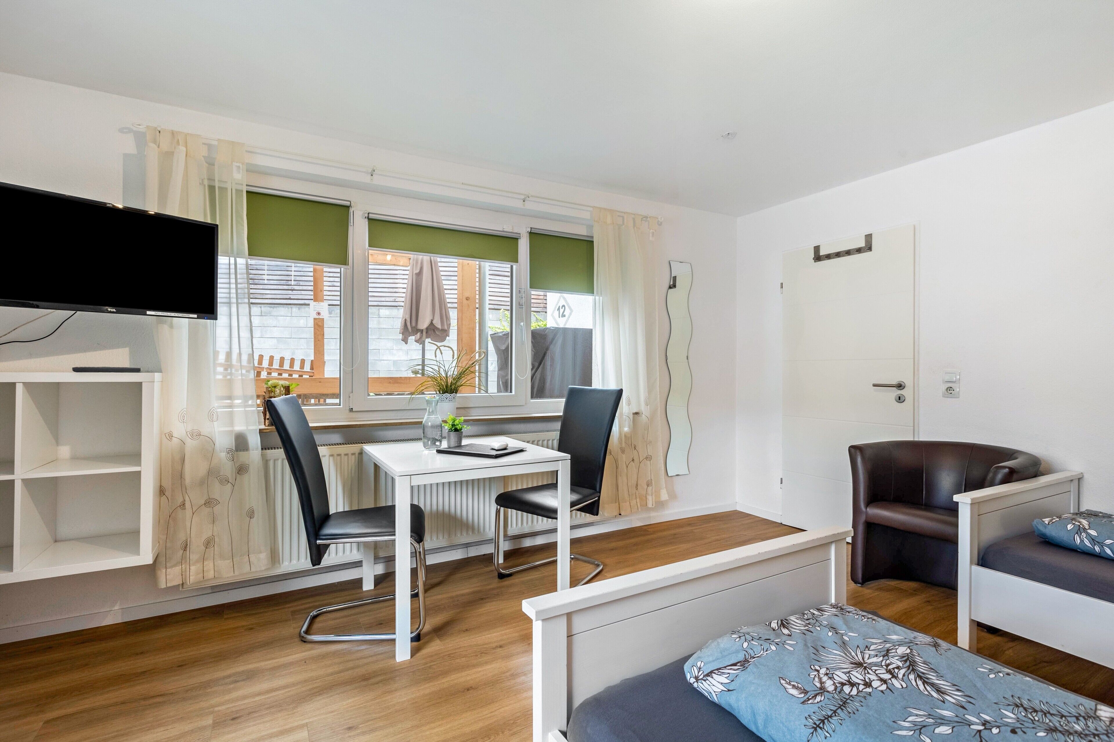 Ein Zimmer mit einem Bett, einem Schreibtisch mit zwei Stühlen, einem Fernseher und einem Fenster mit Vorhängen.