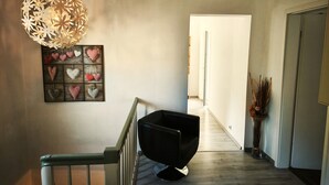 Un couloir doté d’un plancher en bois, d’une chaise noire, d’un luminaire décoratif et d’un élément décoratif en forme de cœur fixé au mur.