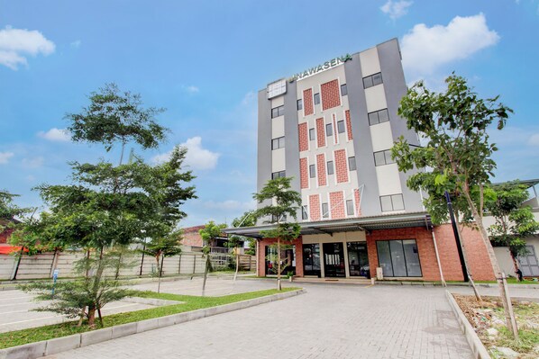 A modern hotel building with a name sign, a paved entrance, and surrounding greenery. - Townhouse Oak near The Park Mall Solo (Grogol)
