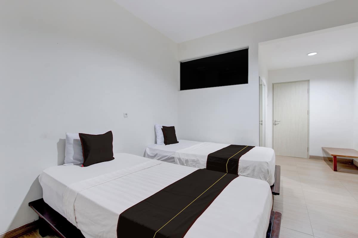 A hotel room with two single beds, a flat-screen TV mounted on the wall, and a wooden bench.
