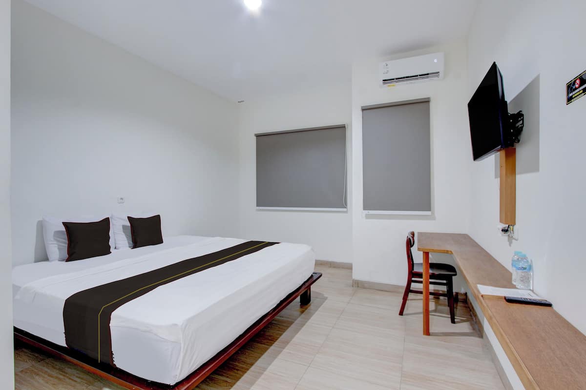 A hotel room with a bed, a desk, a chair, a TV mounted on the wall, and an air conditioning unit.
