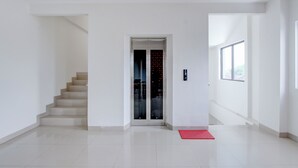 Un hall d’hôtel moderne et vide, avec un escalier, un ascenseur en verre et un tapis rouge.
