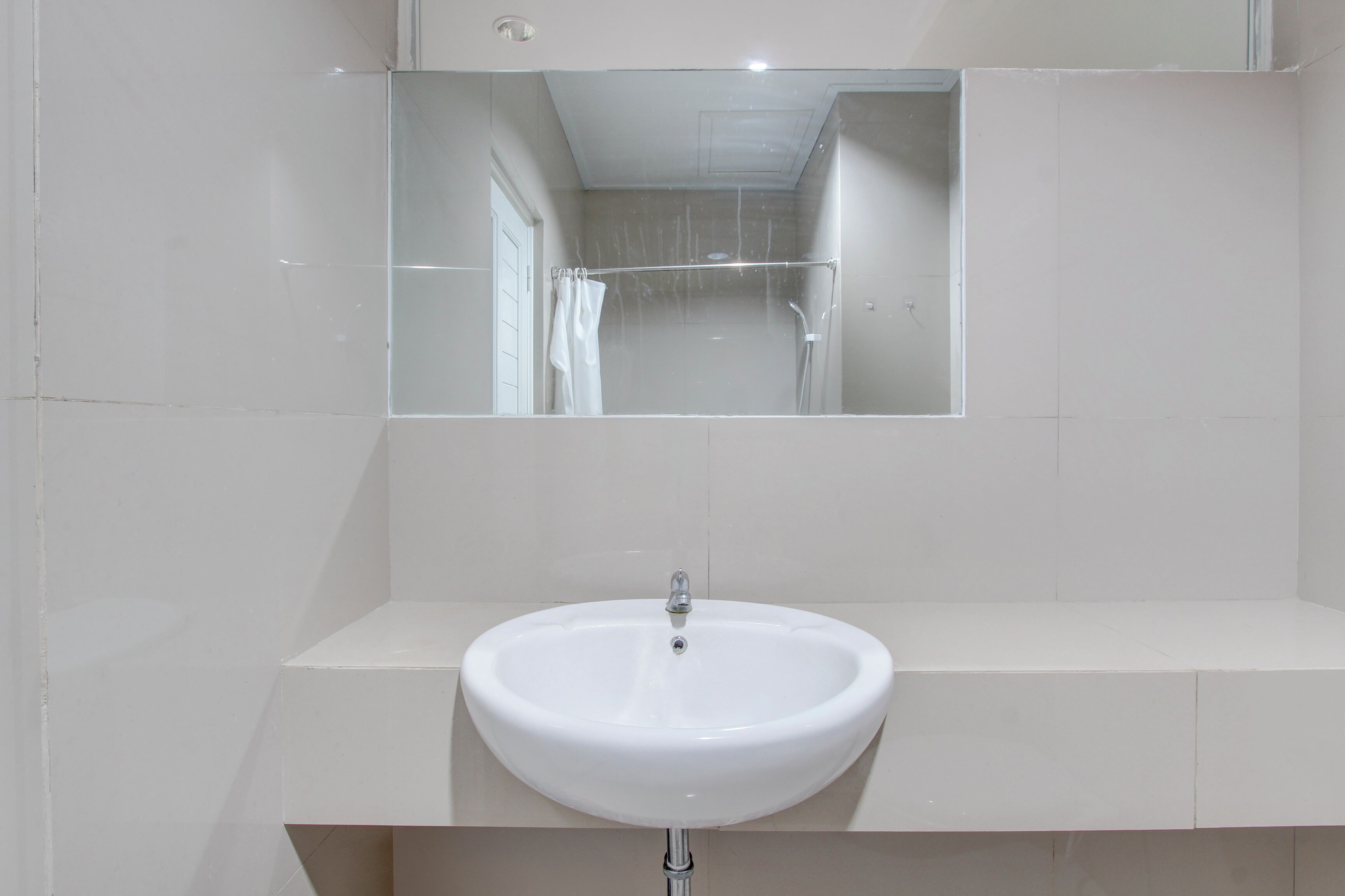 A bathroom with a white sink, a mirror above it, and a shower visible in the reflection.