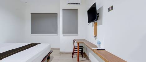 A hotel room with a bed, a desk with a chair, a TV mounted on the wall, and an air conditioning unit.
