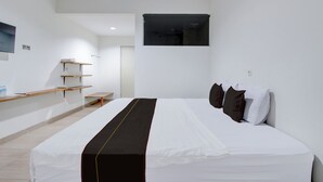 Une chambre d’hôtel moderne avec un grand lit, un petit bureau et un téléviseur fixé au mur.