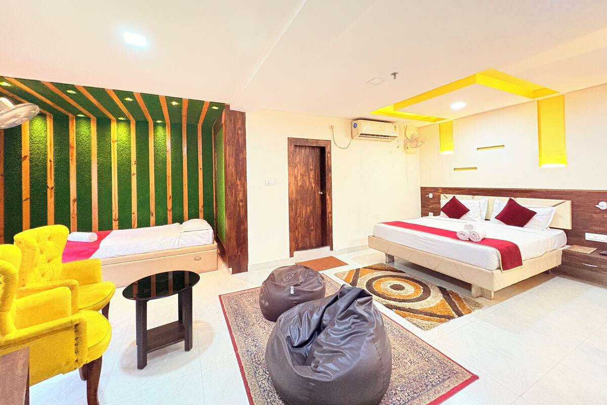 A hotel room with a bed, a yellow armchair, a black ottoman, and a small table.
