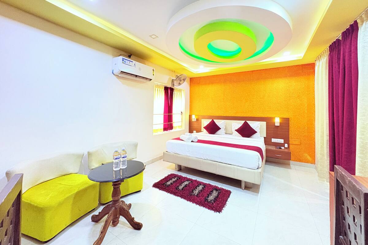 A hotel room with a bed, a yellow sofa, a small round table, and a red rug.