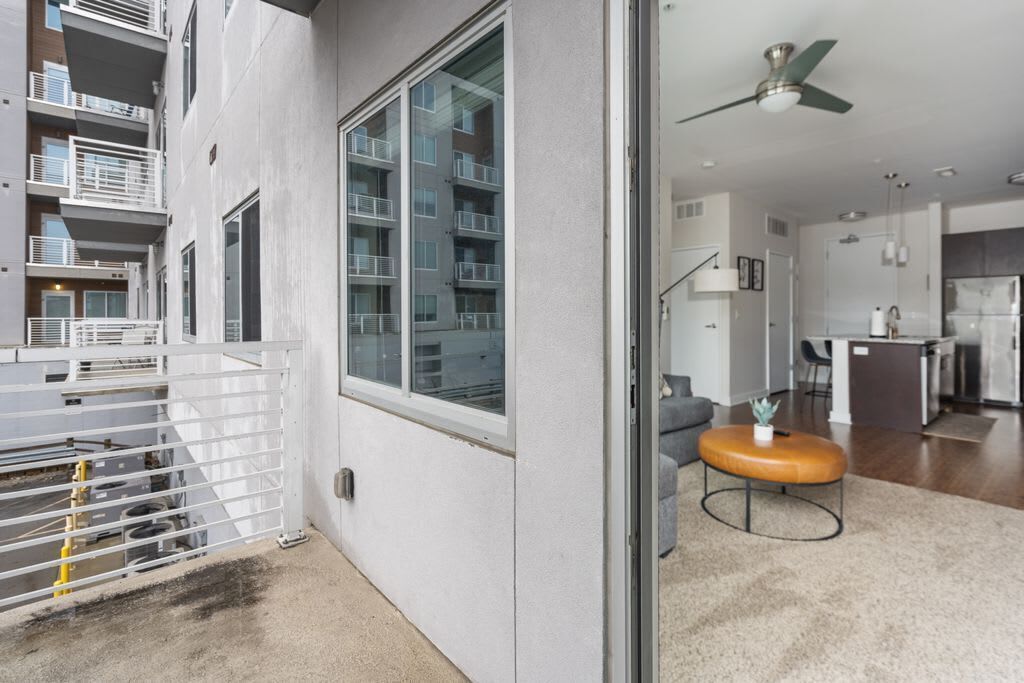 Eine moderne Wohnung mit Balkon, einer Küche und einem Wohnbereich inklusive Sofa und Hocker.