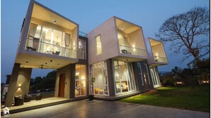 A modern multi-story house with large windows and balconies, featuring a spacious outdoor area with seating. - Suruchi Villa By Soumils Stays (Alibag)