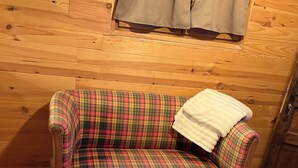 En soffa med rutigt tyg, en vit pläd och en träbänk i ett rum med träpanel på väggarna.