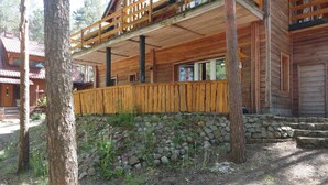 A wooden cabin with a porch, stone foundation, and a view of surrounding trees.