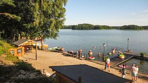 A lakeside beach with a wooden structure, a fenced area, and people engaging in water activities.