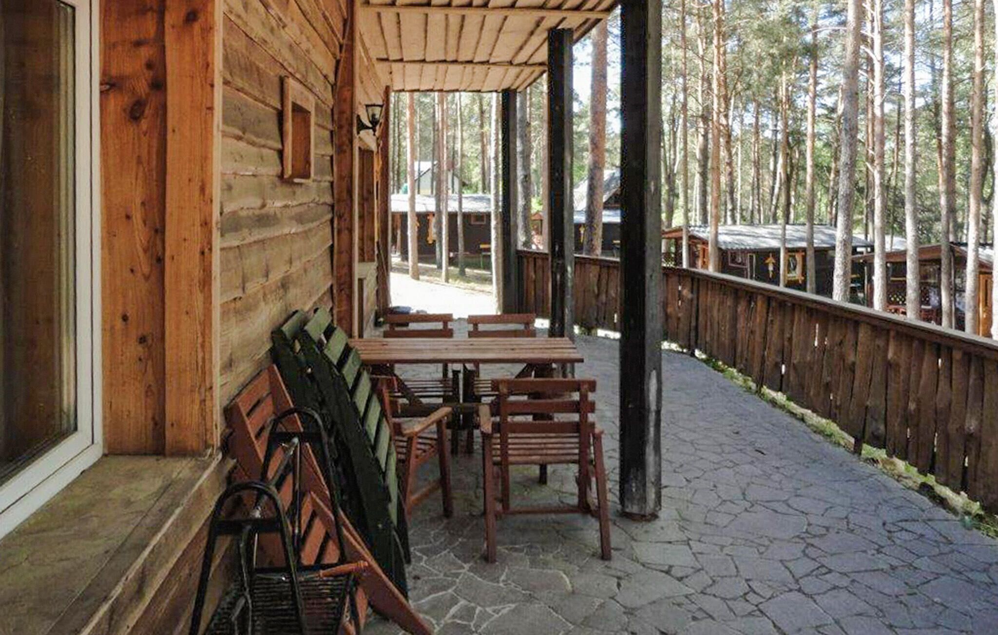 A wooden cabin with a stone patio, wooden benches, and a view of the forest.