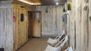 A rustic room with wooden walls, a tiled floor, and a door leading to another area. There are white chairs and a small table with a bottle on the wall.