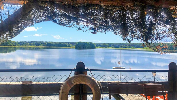 A lakeside view from a covered deck with a lifebuoy, a bench, and a railing. - Beach front home in Ocypel with sauna (Ocypel)