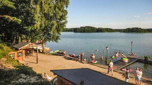 A lakeside setting with a wooden dock, a covered seating area, and a sandy beach. - Beach front home in Ocypel with sauna (Ocypel)