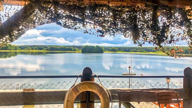 A view of a lake from a covered deck with a lifebuoy, railing, and a lamp post. - Stunning home in Ocypel with sauna (Ocypel)