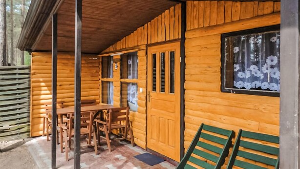 A log cabin with a wooden table and chairs, a door, and a window with a floral curtain.