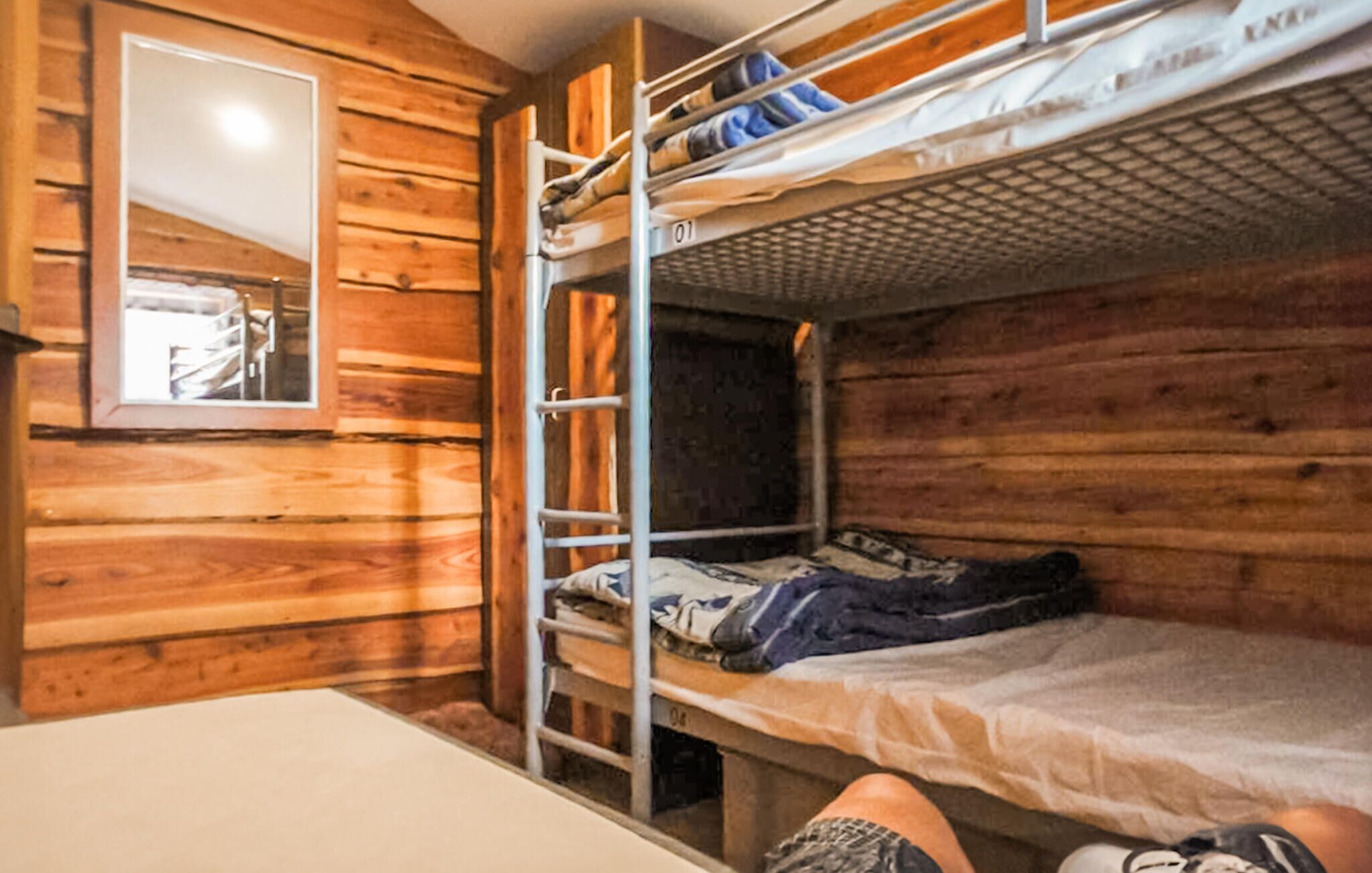 Een slaapkamer met stapelbed, houten wanden, een raam en een metalen ladder.