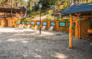 A sandy outdoor area with wooden structures, including a covered seating area with chairs and a wooden fence with picture frames. - Amazing home in Ocypel with sauna (Ocypel)