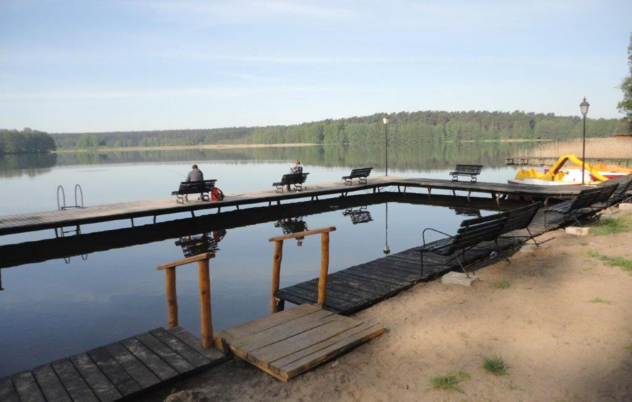 Un muelle de madera que se adentra en un lago tranquilo, con bancos y un pequeño bote.