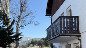 Ein zweistöckiges Gebäude mit einem Balkon, einer Steinmauer und einem gepflasterten Weg, der zu einer Holztür führt.