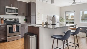 Una cocina moderna con armarios oscuros, electrodomésticos de acero inoxidable, una encimera de granito y taburetes de bar.