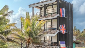 A multi-story building with a balcony, palm trees, and flags. - Secret Beach Ahangama Galle (Ahangama)