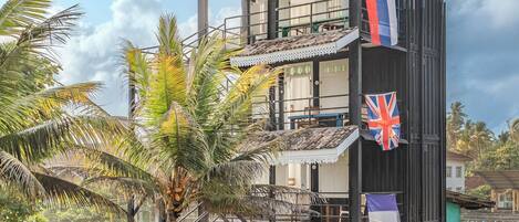 A multi-story building with a balcony, palm trees, and flags.