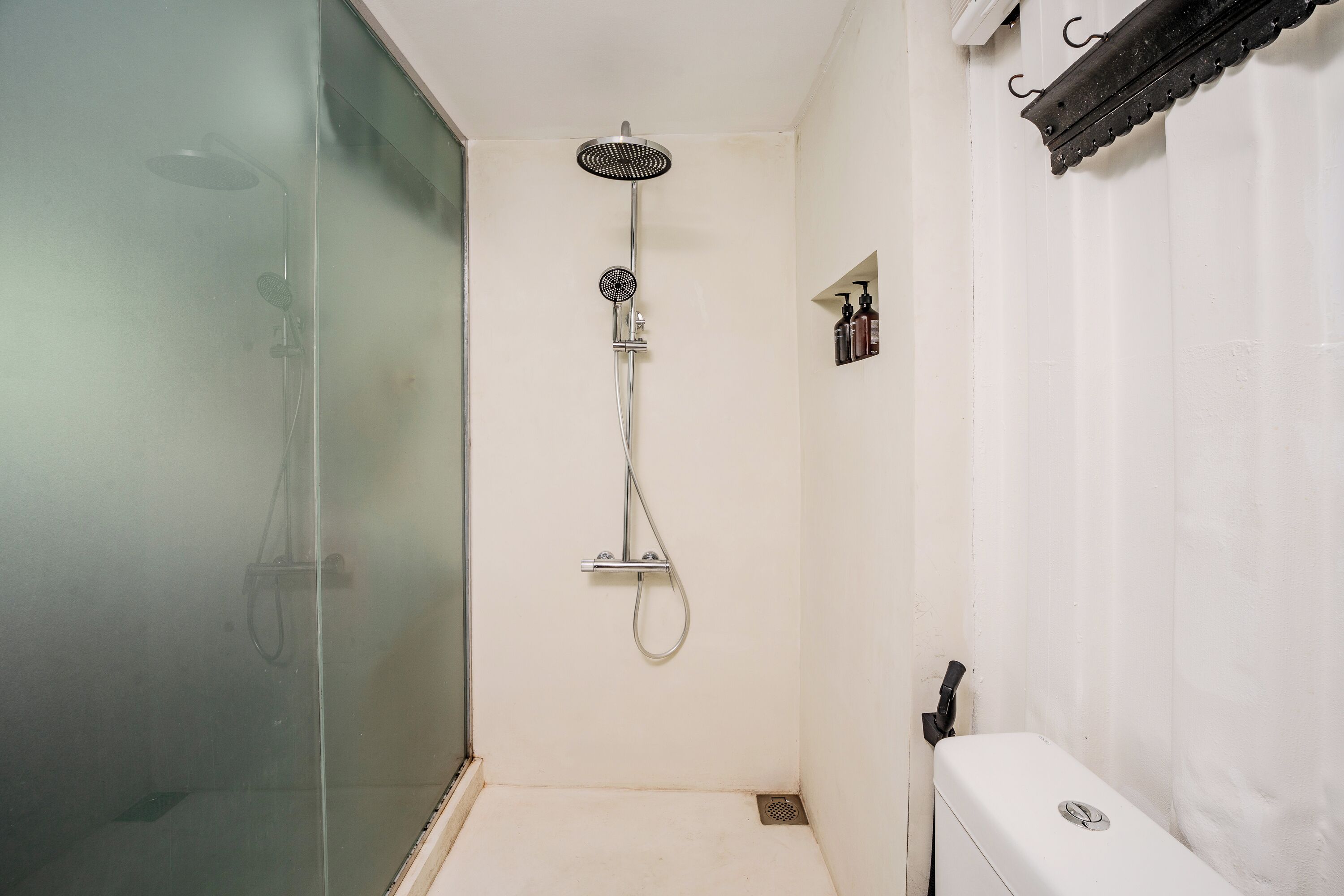 A small, enclosed shower area with a glass door, a handheld showerhead, and a wall-mounted faucet.